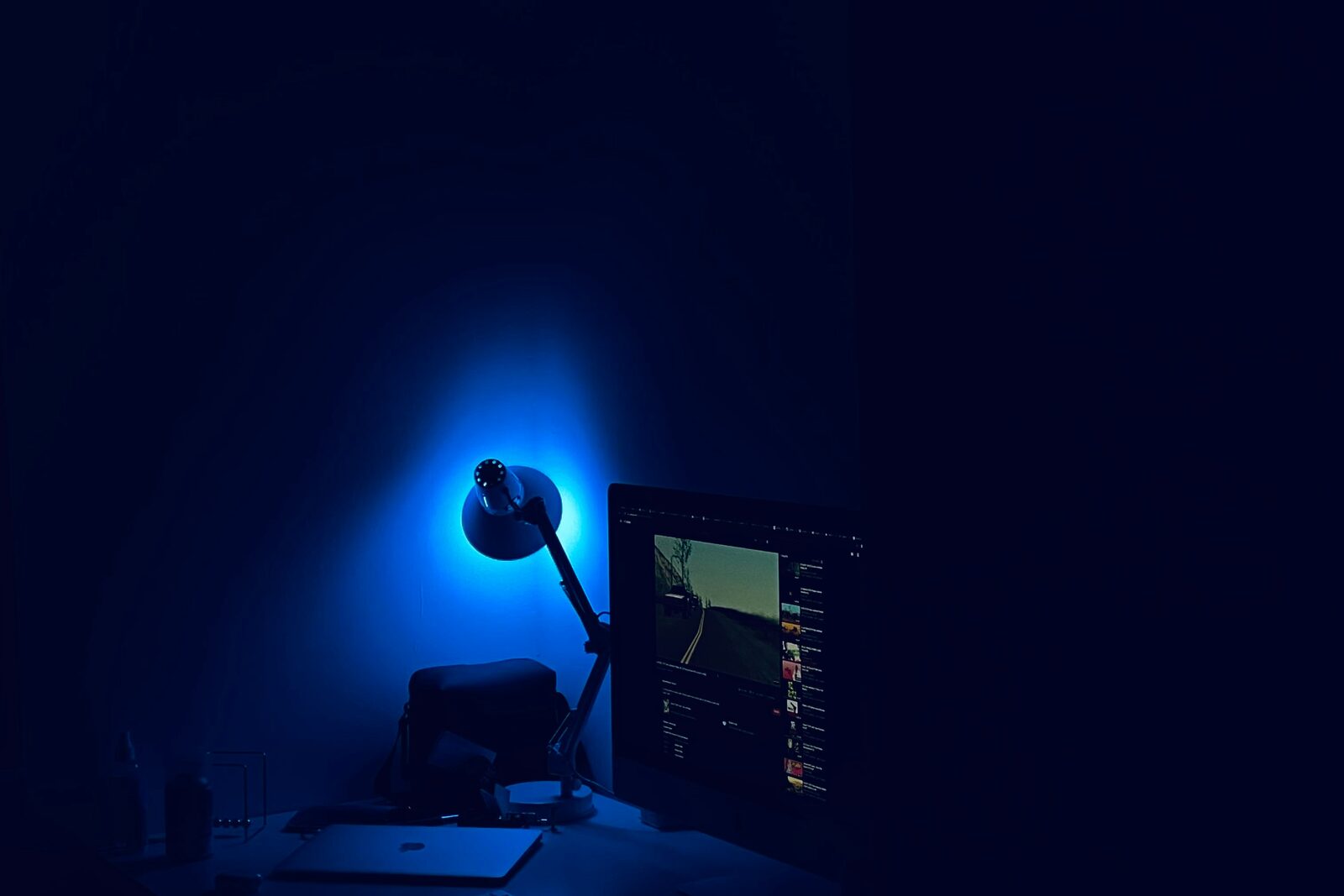 Ein Schreibtisch bei Nacht, von einer Lampe blau ausgeleuchtet, daneben ein Monitor.